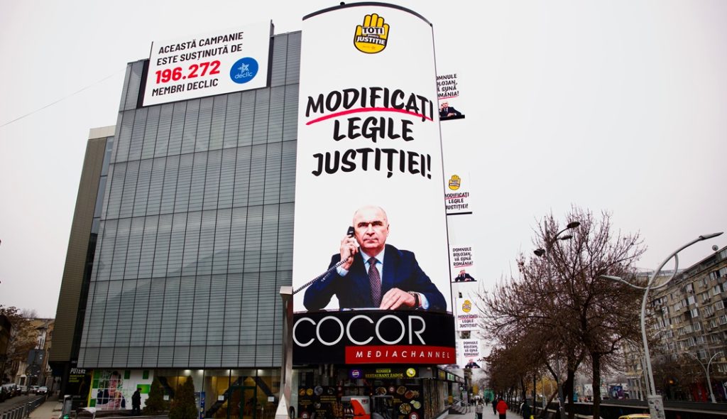 O reclamă imensă pe fațada magazinului Cocor din București, afișând o fotografie a premierului Bolojan și mesajul „Schimbați legislația justiției”