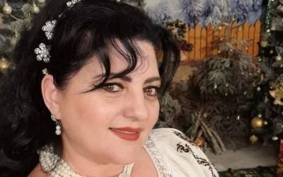 Imagine de prim plan cu Mihaela Cojocaru, cu o bentiță cu flori în păr, iar pe fundal un decor de Crăciun